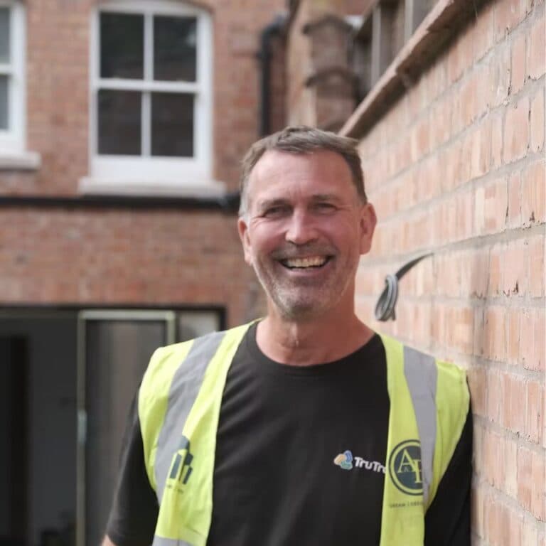 Tony from TruTrade wearing a high-visibility vest and smiling in front of a brick building