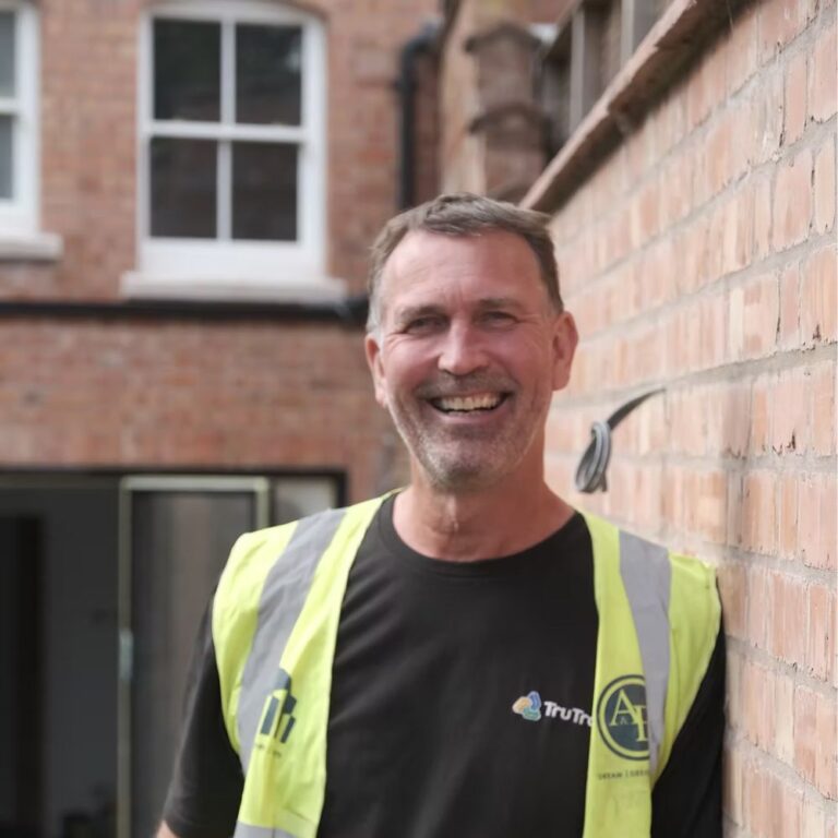 Tony from TruTrade wearing a high-visibility vest and smiling in front of a brick building