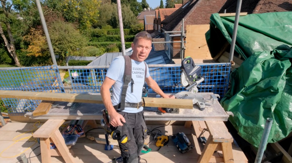 A carpenter at a mitre saw on a scaffold platform