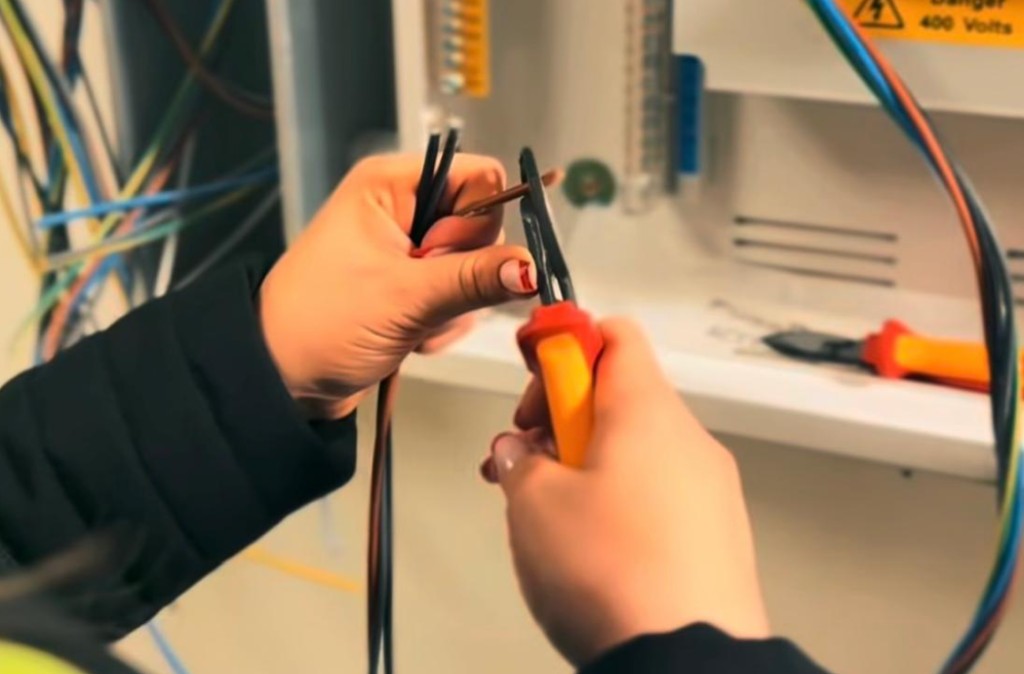An electrician stripping cable at a distribution board