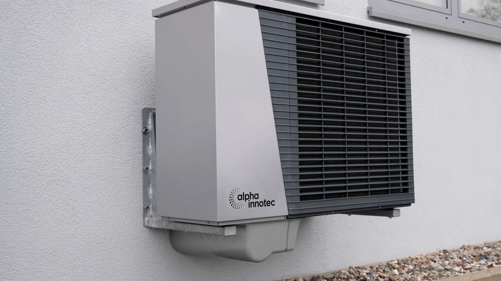 A wall-mounted air source heat pump on a rendered exterior wall