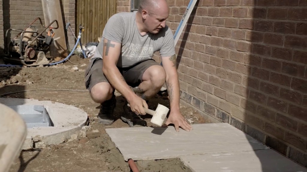 A landscaper bedding a patio slab with a rubber mallet