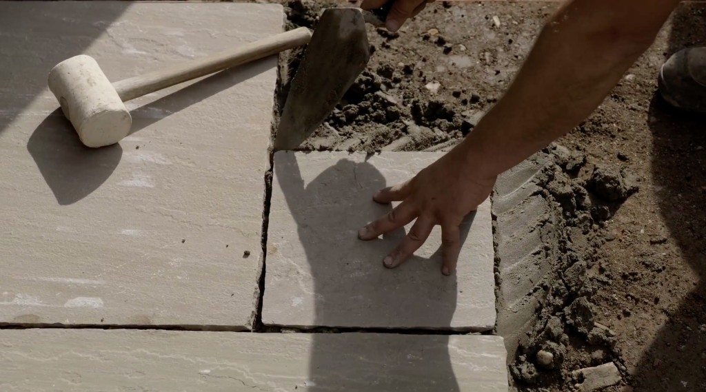 A hand setting a patio slab on a sand bed