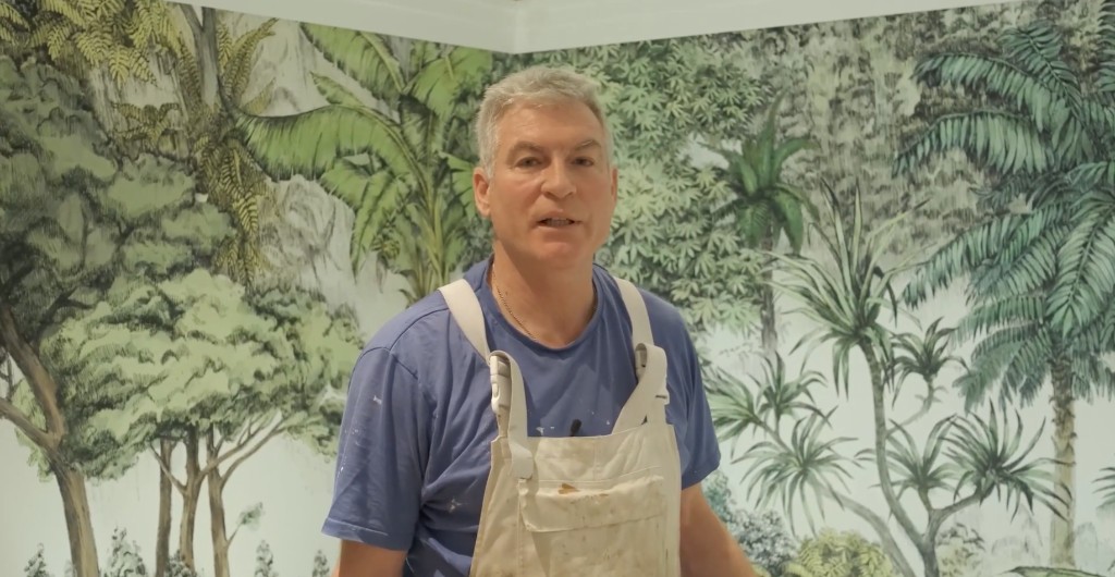 A decorator in overalls in front of a finished mural