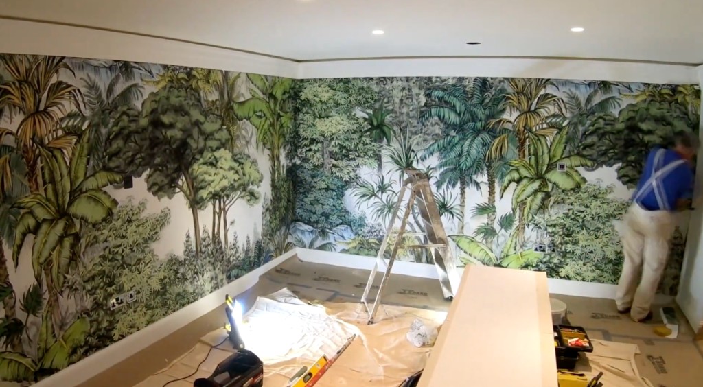A decorator hanging a jungle mural in a living room