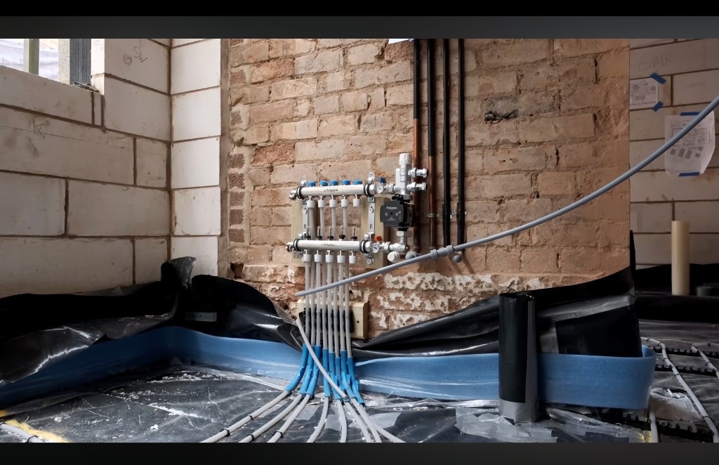 A heating manifold and pipework on a brick wall during first fix