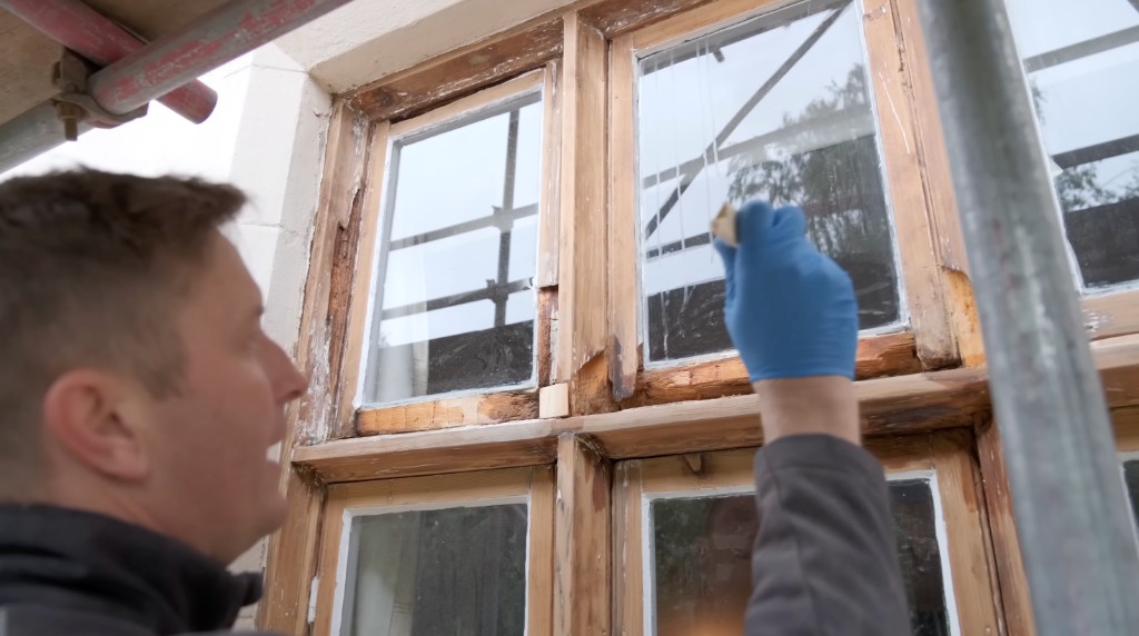 A glazier working on a timber sash from a scaffold